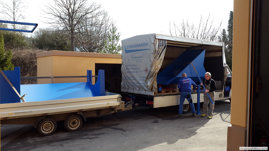 Blaues Metallbauteil auf einem Anhänger neben einem geöffneten Lkw.