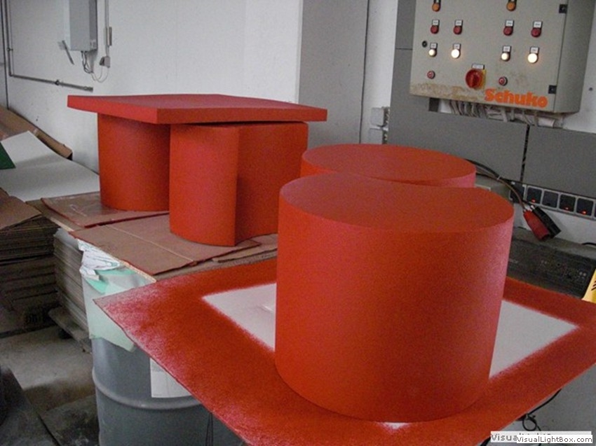 Orangefarbene zylindrische Bauteile und rechteckige Platten auf Arbeitsflächen.