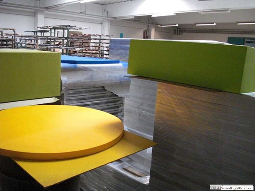 Gelbe runde Platten und grüne rechteckige Bauteile in einer Werkhalle.