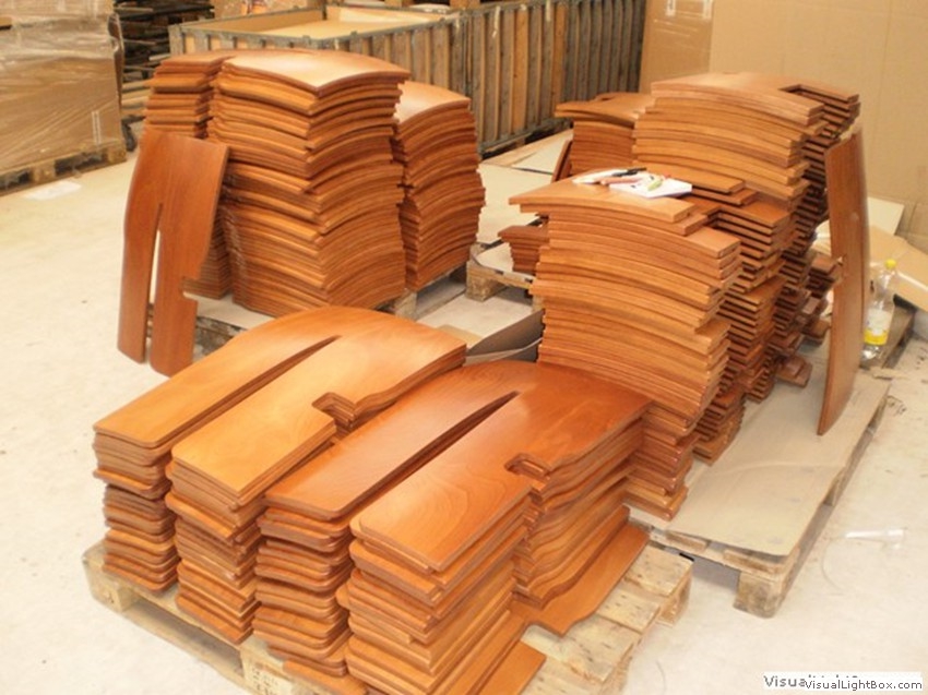 Gestapelte braune Holzteile mit geschwungenen Konturen auf Paletten.