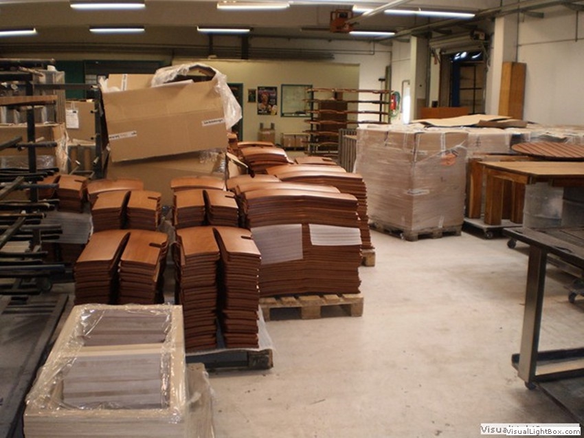 Braune Holzbauteile, Kartons und verpackte Paletten in einer Werkhalle.