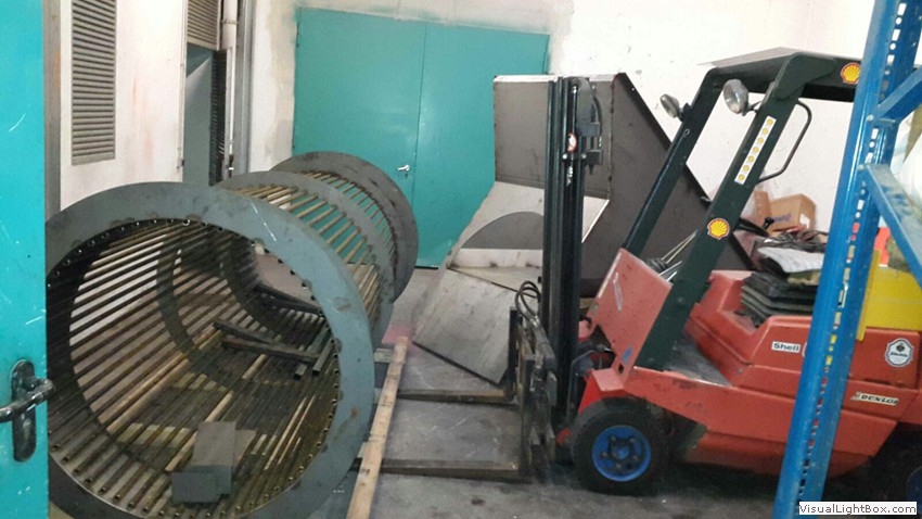 Große zylindrische Gestelle mit Metallringen und Holzstäben neben einem Gabelstapler.