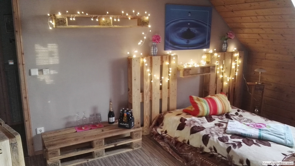 Bett mit einer beleuchteten Rückwand und Ablageflächen aus Holzpaletten.