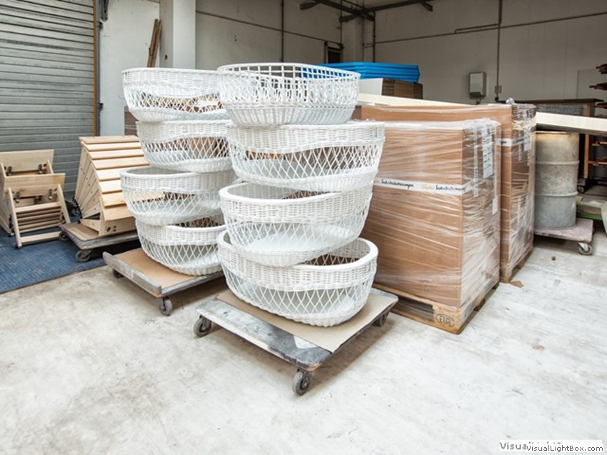 Weiße Flechtkörbe, auf einem Wagen gestapelt, neben verpackten Paletten.