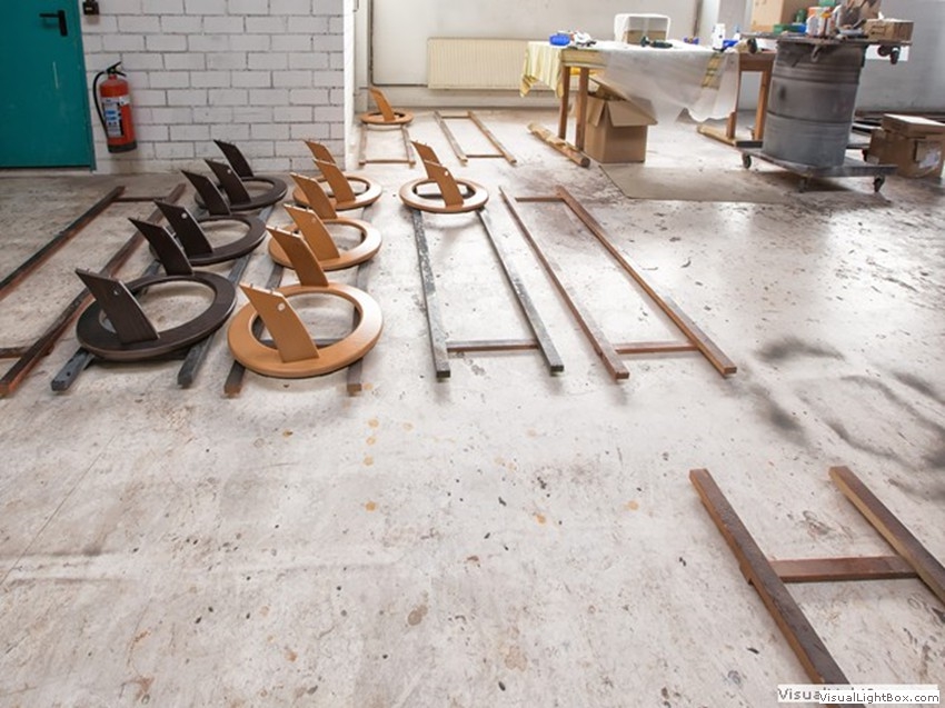 Runde Möbelbauteile und lange Leisten in hellen und dunklen Holztönen auf dem Werkstattboden.