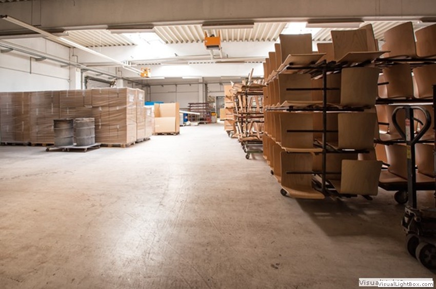 Heller Gang in einer Werkhalle zwischen verpackten Paletten und Transportgestellen.