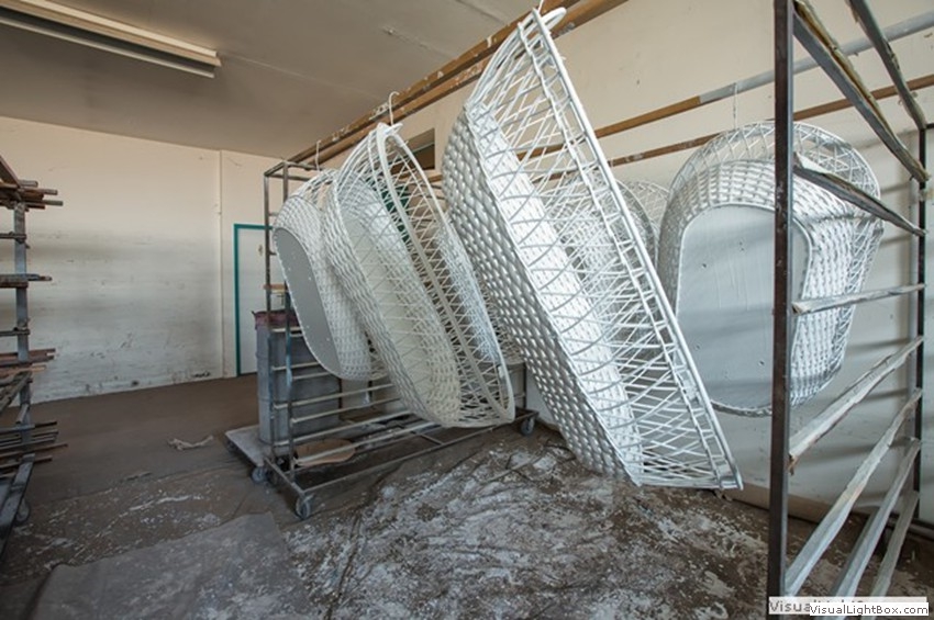 Weiße geflochtene Möbelbauteile, hochkant an einem Metallgestell aufgehängt.
