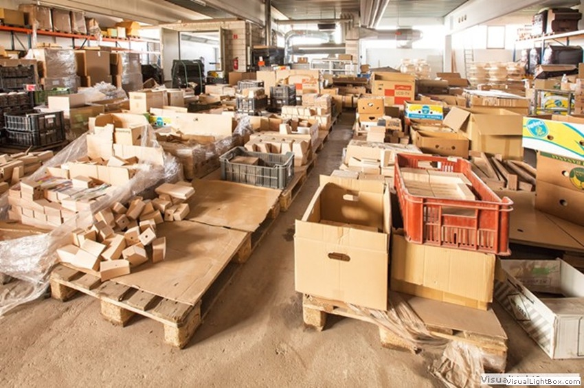 Werkhalle mit Kartons, Holzbauteilen und Transportbehältern auf Paletten.