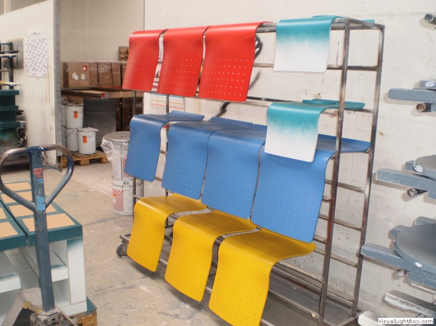 Rote, blaue und gelbe Sitzschalen mit Lochmustern auf einem Metallgestell.