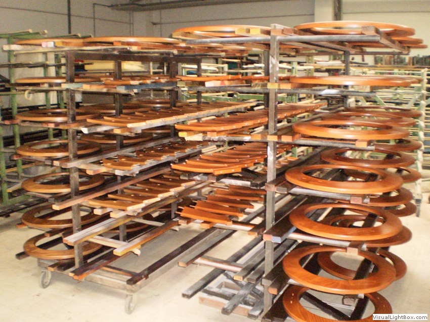 Braune ovale Holzrahmen und weitere Holzbauteile auf dicht bestückten Transportgestellen.
