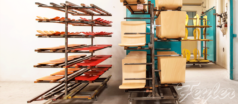Transportgestelle mit rötlichen Leisten und hellen Sitzschalen in einer Werkstatt.
